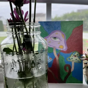 A glass jar with flowers in it next to a painting.