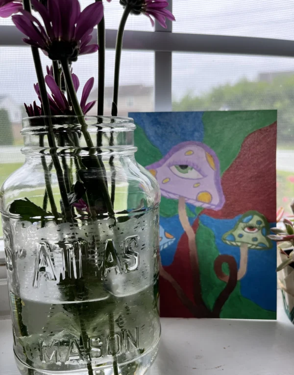 A glass jar with flowers in it next to a painting.