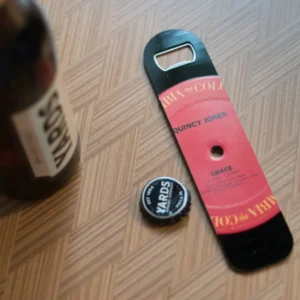 A bottle opener and beer cap on the floor.