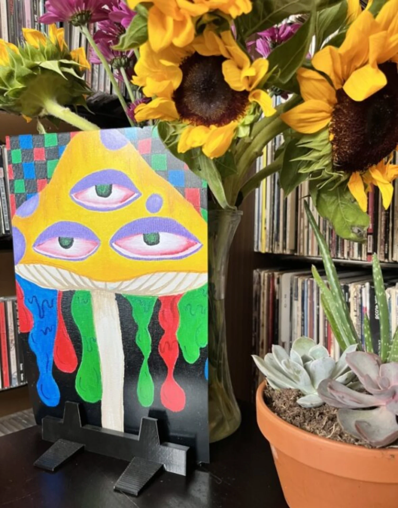 A painting of a face with eyes on it next to a plant and a book.